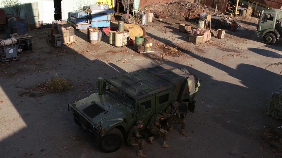 Major and two of his coworkers hide behind a Humvee in the middle of a bunch of junk.