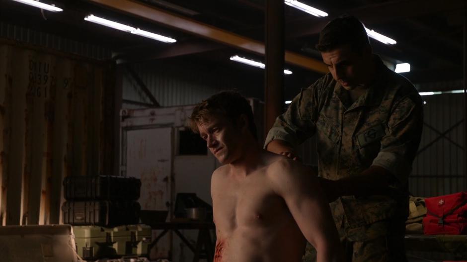 One of Major's fellow mercenaries patches up his gunshot wound.