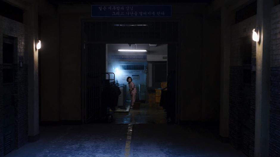 Min-Jung looks up from where she is mopping at the end of the hall after Sun is escorted past.