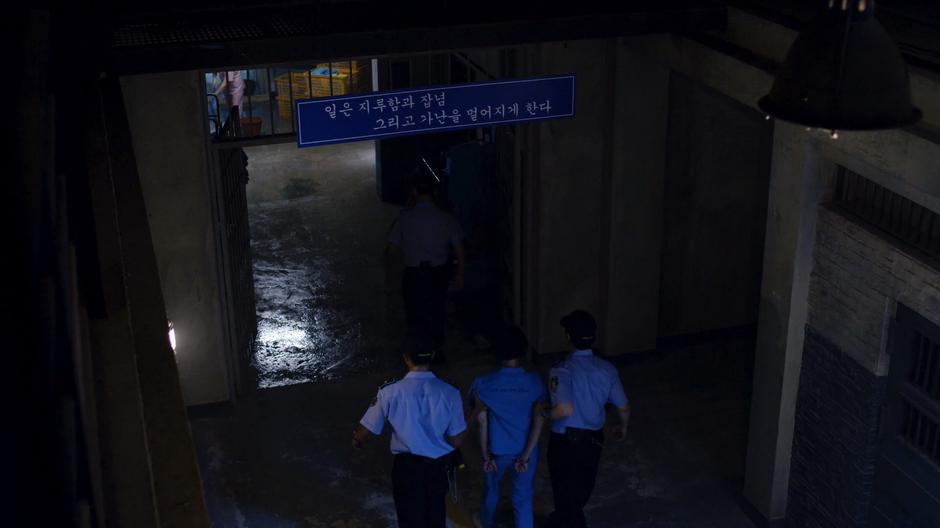 A guard walks ahead while two others escort Sun down the main hall of the prison.