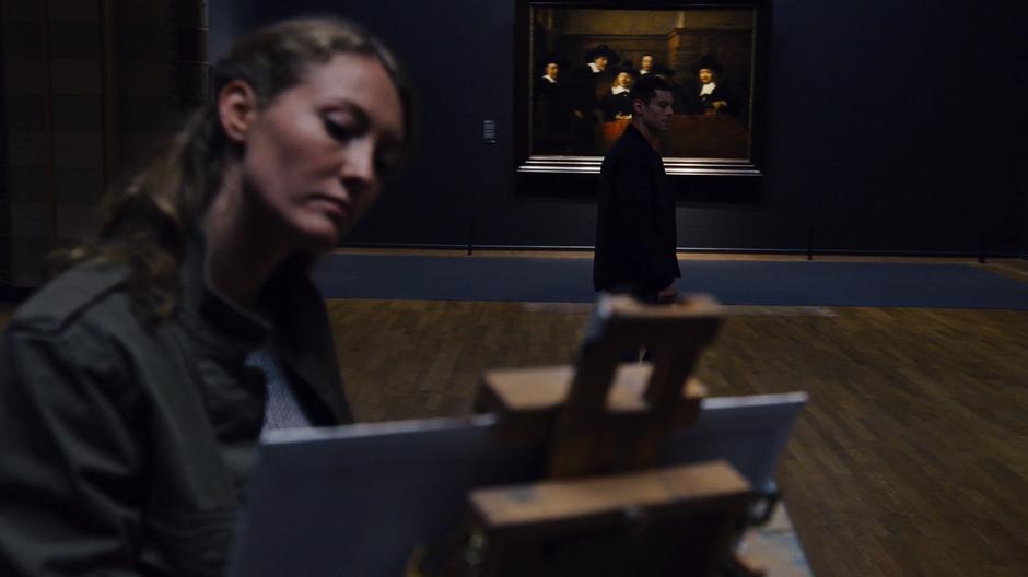 Will walks past a woman who is painting one of the paintings.