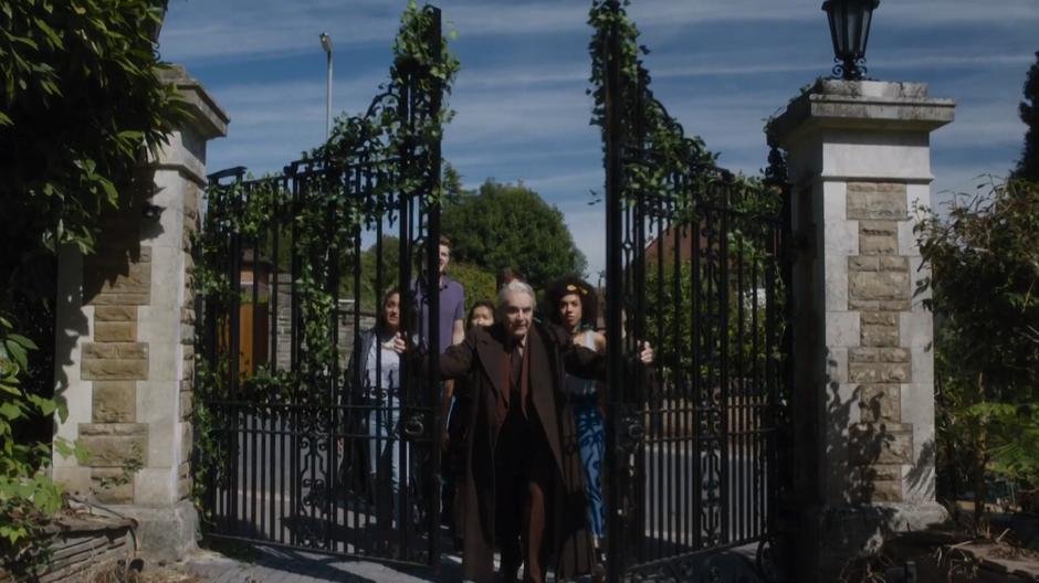 The landlord pushes open the gate leading to the house while the students follow behind.