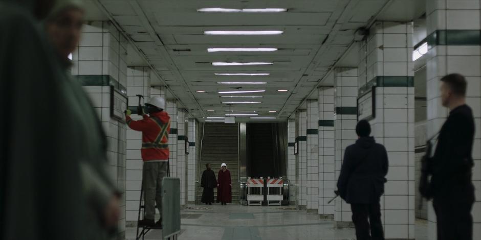 Moira and June walk down onto the subway platform while a worker removes the signage.