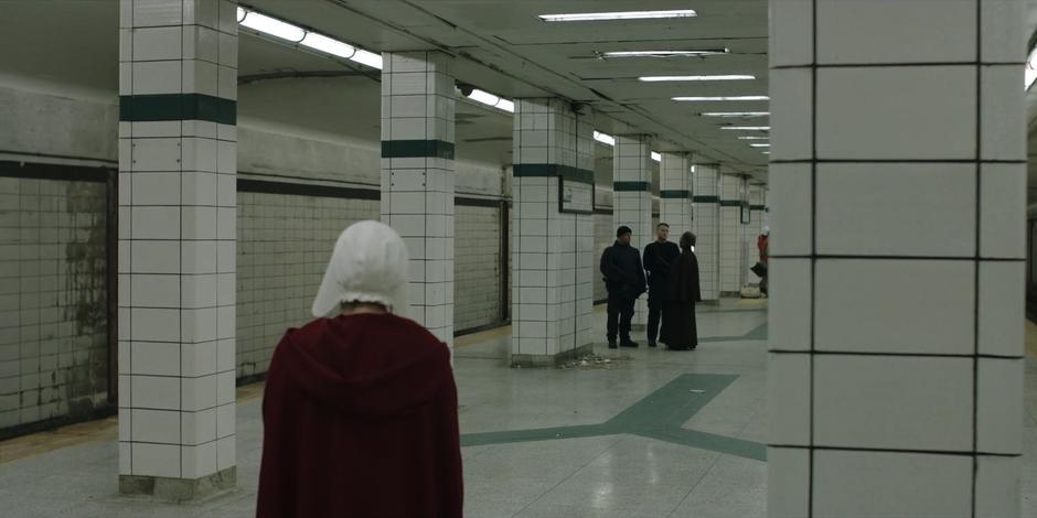 June stands around while Moira talks to a pair of guards looking for directions.