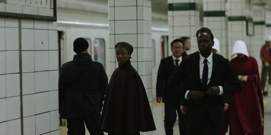 Moira looks back at June while travelers exit the train.