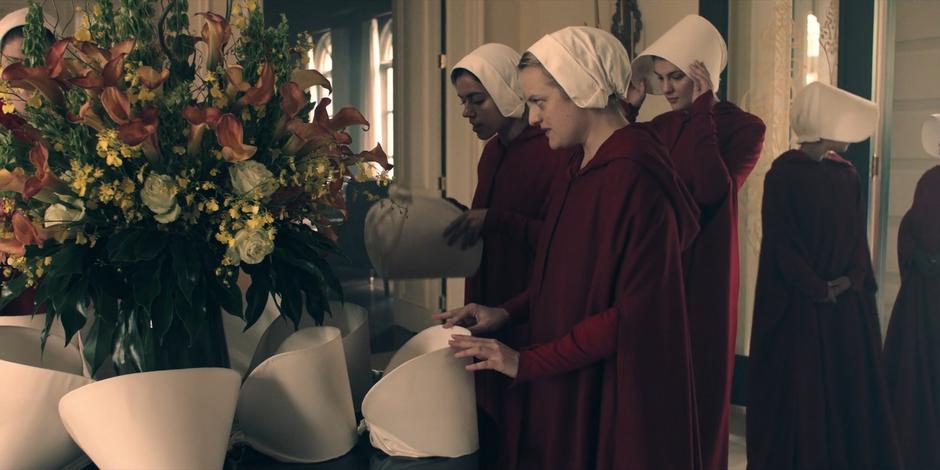 Offred and the other handmaids take off their hats in the front hall.