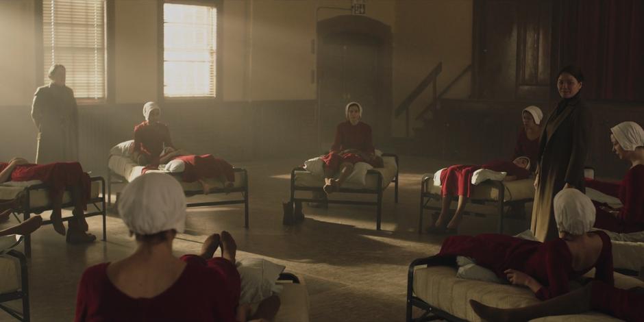 The handmaids-in-training lie on the beds in a circle while Aunts Lydia and Elizabeth teach them about the Ceremony.