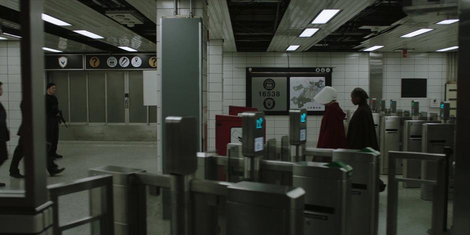 June and Moira pass through the payment area past several guards.