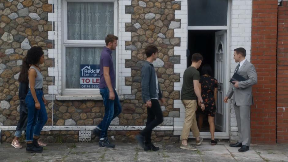 The estate agent stands by the door while the students file in.