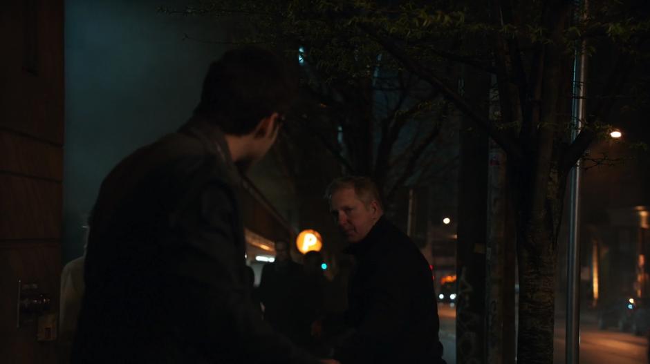 Mon-El turns around after being bumped by a man walking past.