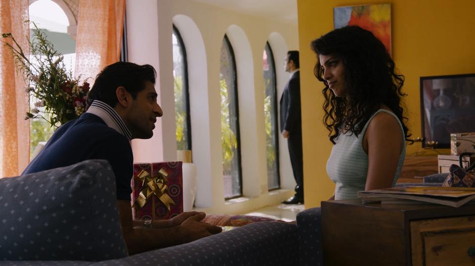 Ajay talks to Kala about missing her wedding while they sit on the couches and Kala's guard stands in the background.
