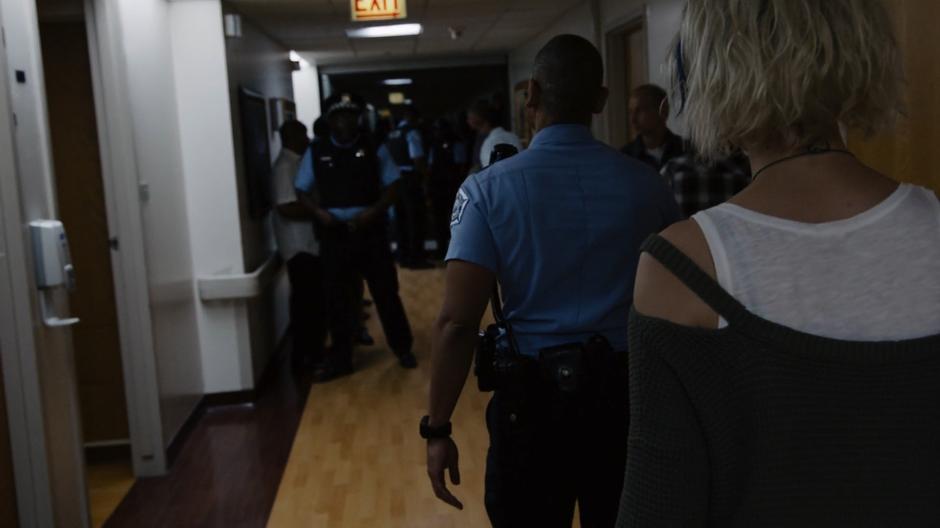 Diego walks down the hospital corridor with Riley following through the assembled police officers.