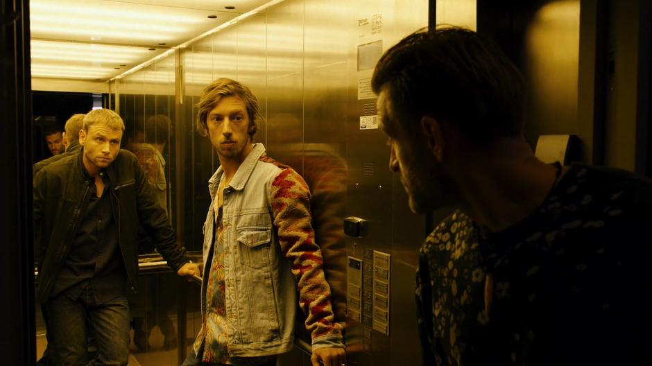 Wolfgang and Felix look out of the elevator as they are ushered in by Sebastian Fuchs's guard.