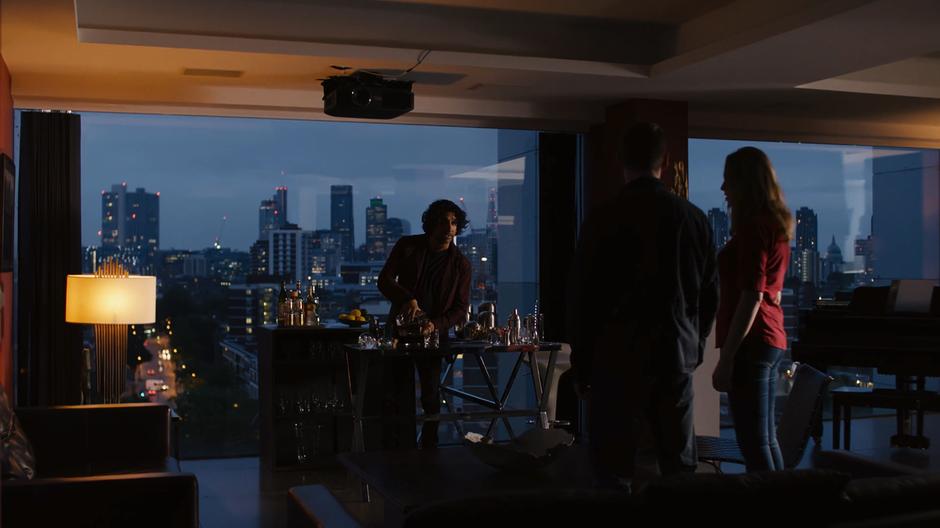 Jonas pours himself a drink in front of the London skyline while explaining his surprise survival to Will and Nomi.