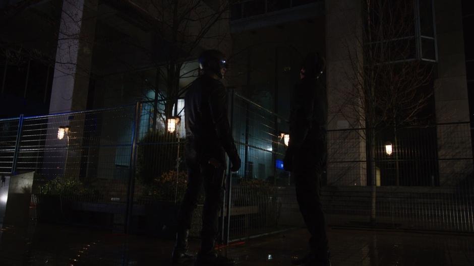 Diggle and Oliver stand in front of the fenced off building.