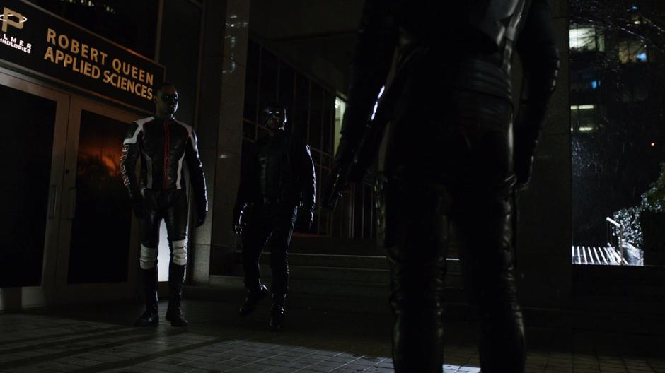 Oliver approaches Curtis and Diggle in front of the doors to the building.