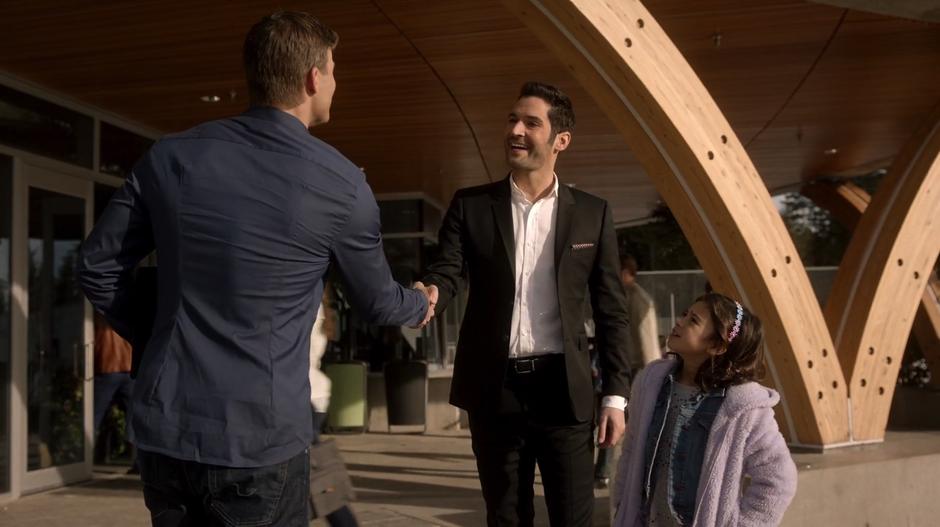 Lucifer shakes Mr. Taylor's hand out front of the school while presenting Trixie as his daughter for the tour.
