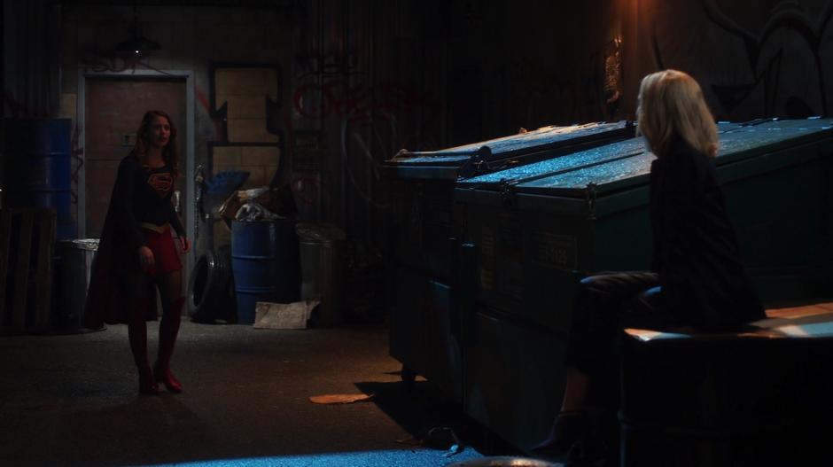 Kara turns around to see Cat Grant sitting on some barrels in the alley outside the bar.