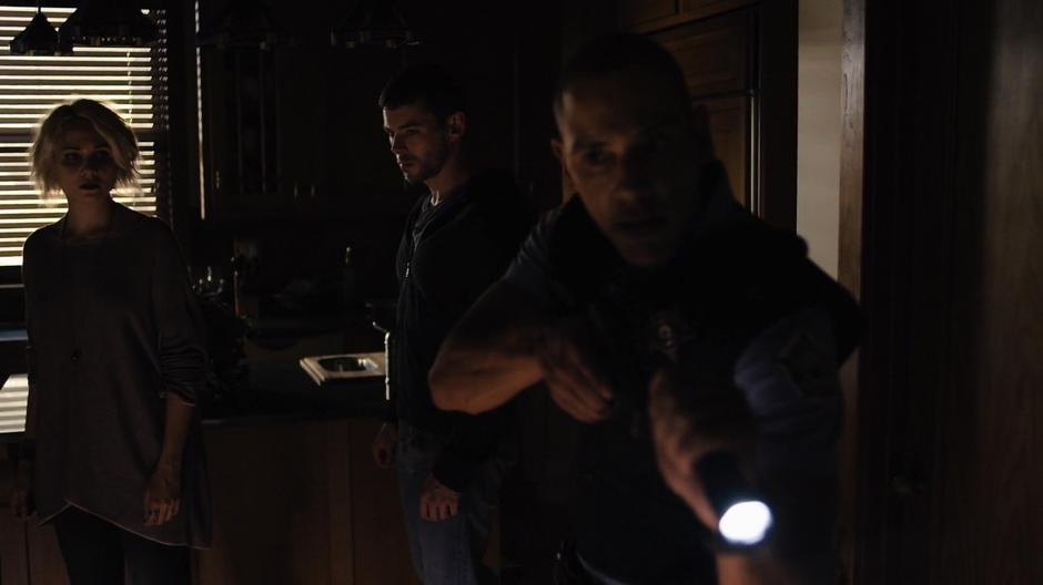 Diego shines his flashlight around the house while Riley and Will follow behind him.