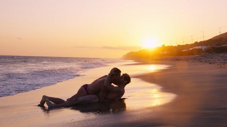 Hernando and Lito kiss while lying in the surf with the sun setting behind them.