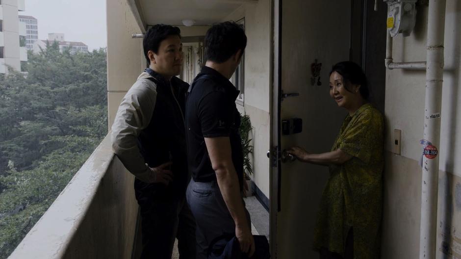 Mrs. Cho talks to Detective Mun and his partner out front of the apartment.