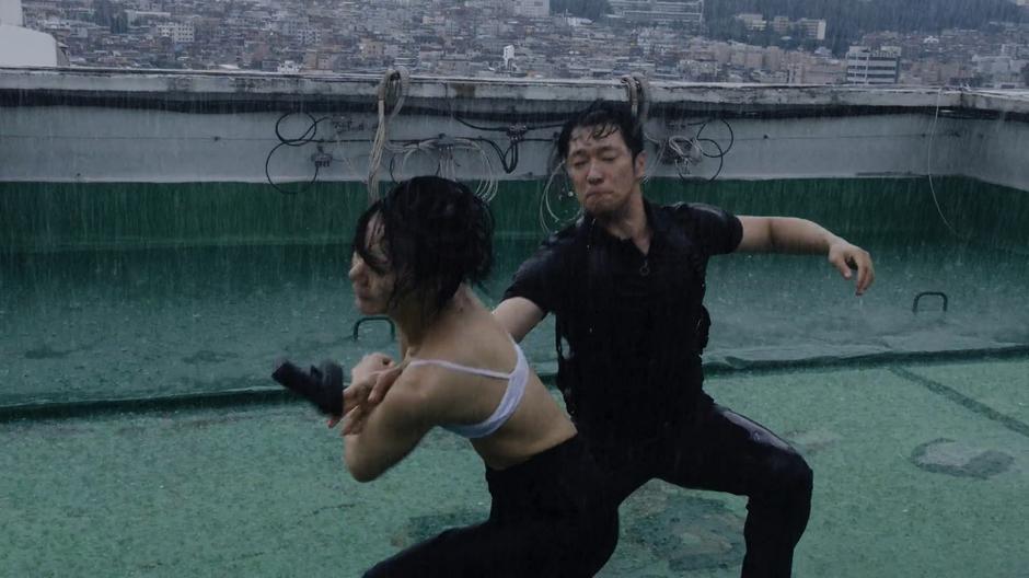 Sun knocks the gun out of Detective Mun's hand while they fight on the rooftop in the rain.