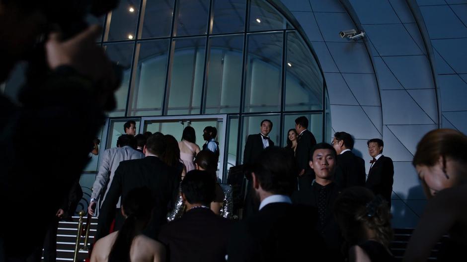 Joong-Ki walks up the front steps of the building surrounded by guards and his entourage.