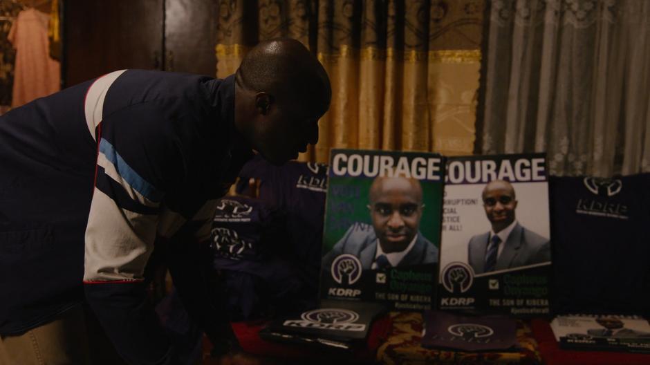 Capheus looks down at the campaign posters and sees his mother asleep on the floor.