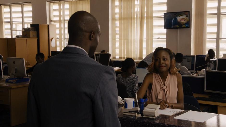 Capheus approaches the receptionist at the news company who smiles at him as he asks about Zakia.