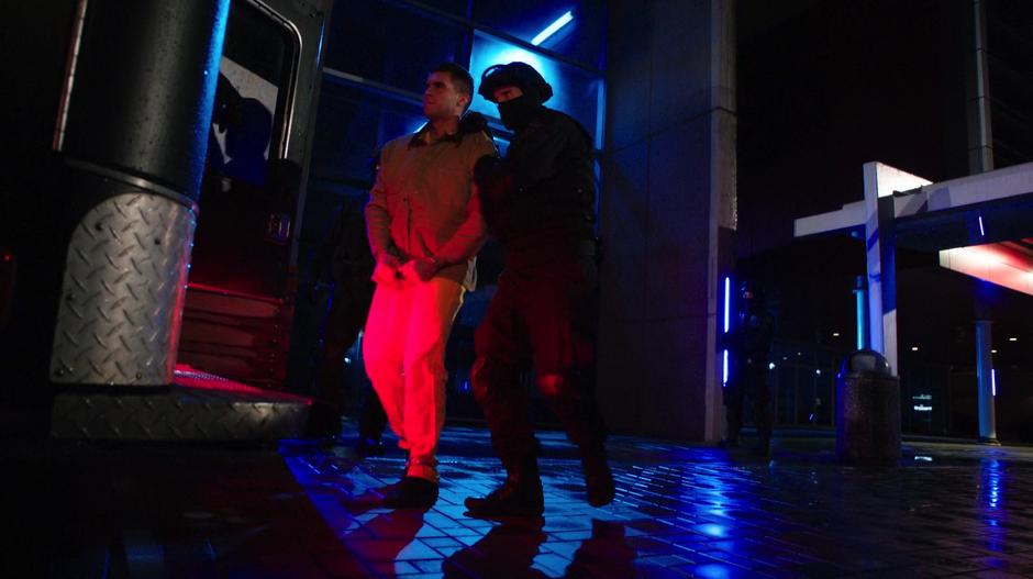 Adrian Chase is escorted by an A.R.G.U.S. agent into the transport truck.
