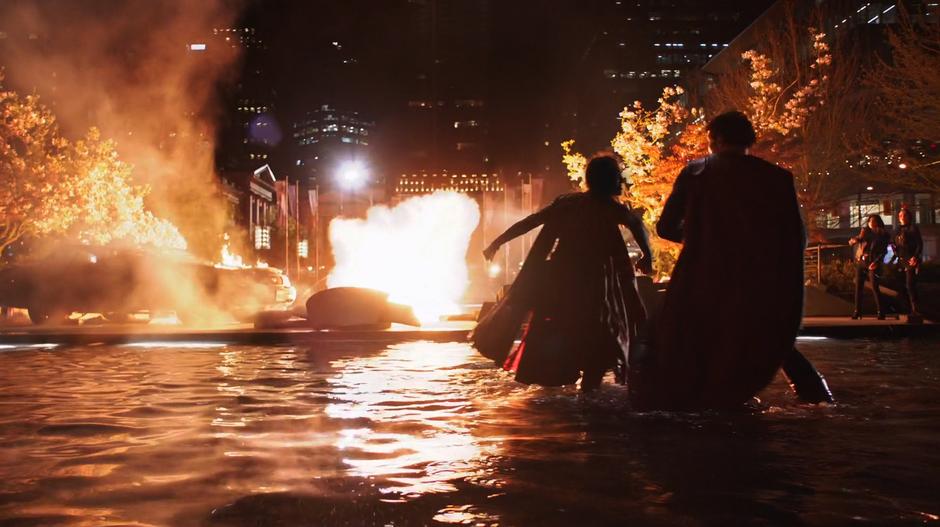 Kara and Clark fight in the shallow pond while Alex and Maggie watch from the background and an explosion rocks the square.