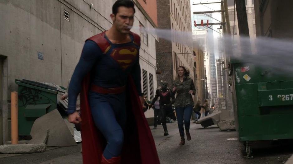 Clark uses his freezing breath to fight off some Daxamites while J'onn runs up from the alley.