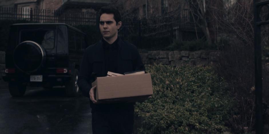 Nick carries a box of books out of the house to the trash on the curb.