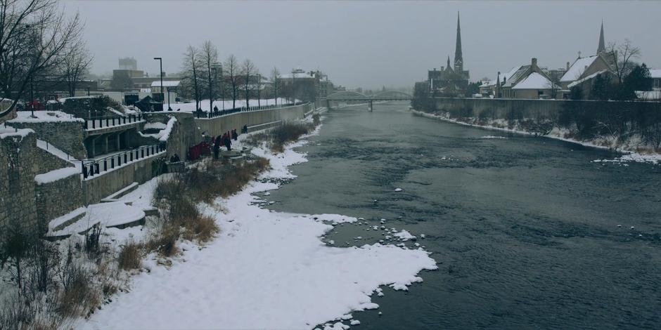 A view over the river and snow covered landscape as the handmaids work along the river path cleaning up blood.