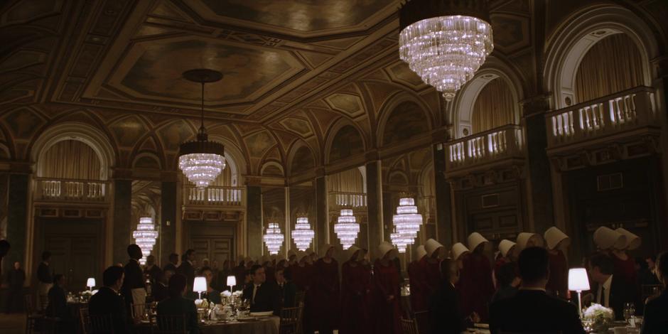 The handmaids file into the ballroom in two orderly lines.