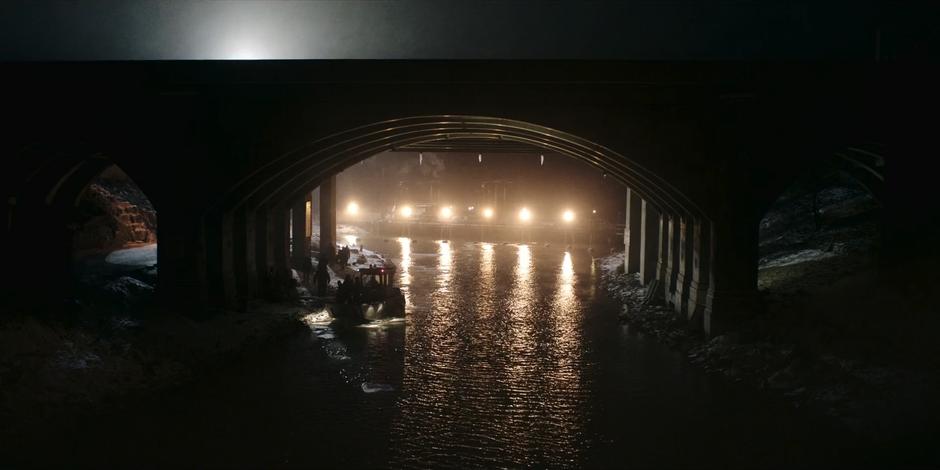 The smuggling boat sits docked underneath the bridge while being illuminated by a series of spotlights on the dock.
