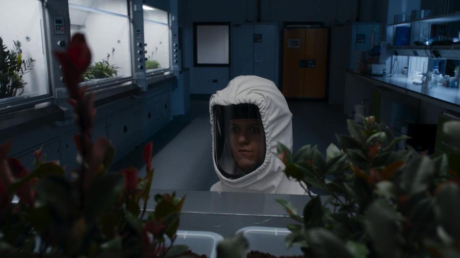Erica looks at the plants in the testing room while wearing a protective suit.