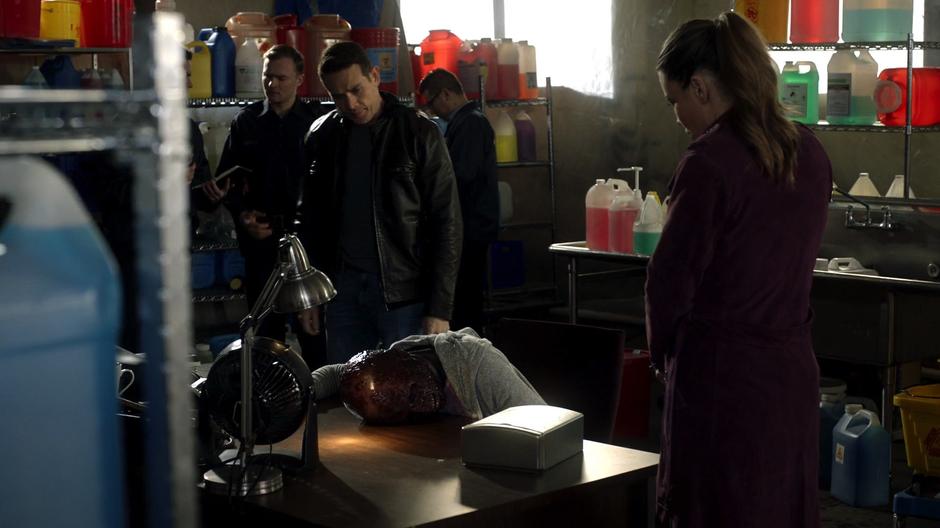 Dan and Chloe examine the burned body of Ava Lyon who is lying at her desk.