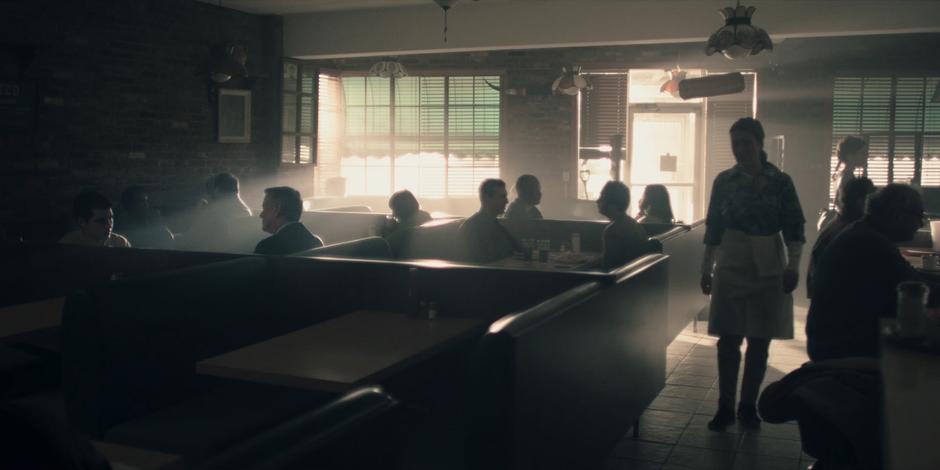 Nick and Andrew Pryce talk at a booth in the diner while a waitress walks around serving people.