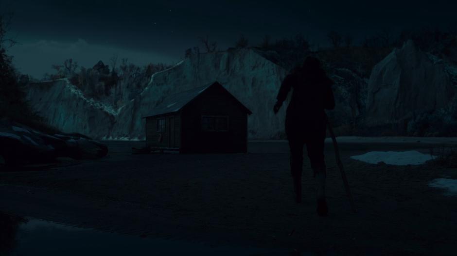 Sarah walks across the sand to the boathouse at night.