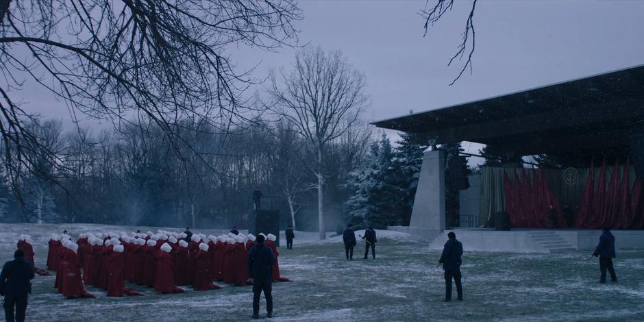 Two guards hammer in a spike in front of the stage where the handmaids are assembled.