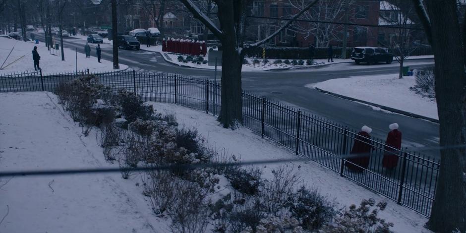 Offred and Ofglen walk across the street to where the rest of the handmaids are waiting.