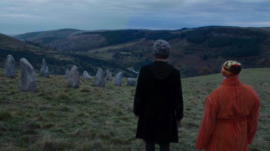 The Doctor and Nardole look at the line of stones leading up to the cairn.