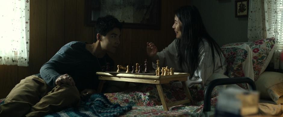 Zack's mom smiles at him as they lay on the bed playing a game of chess.