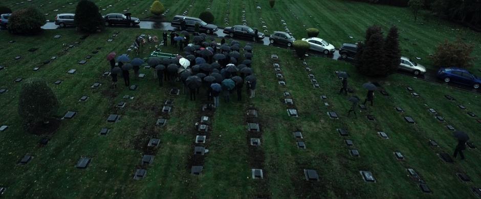 Mourners stand around the grave holding umbrellas during the funeral.