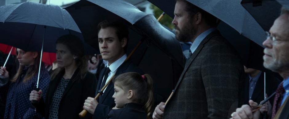 Jason looks over at Kimberly while standing with his sister and father at the funeral.