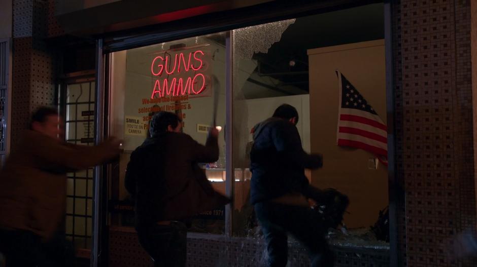 Several people break the front window of a gun store and leap inside.