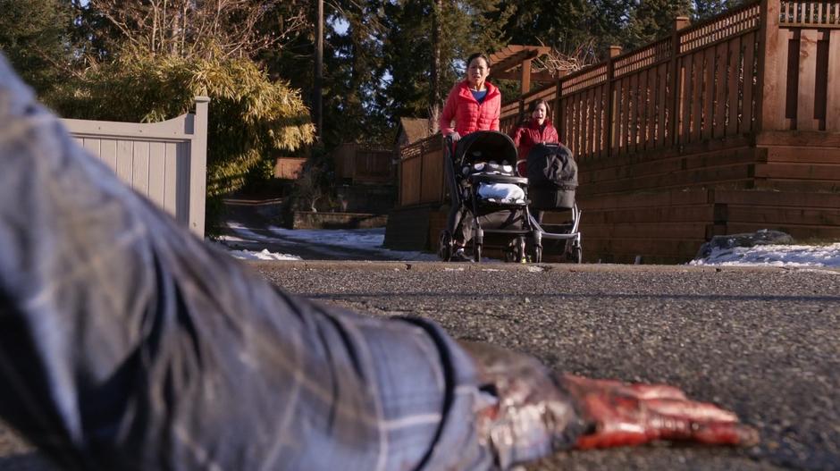 Two women with stroller see half of a zombie crawling down the street.