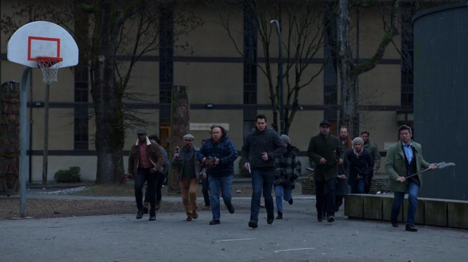 Mob of armed humans run across the park towards the group of zombies.