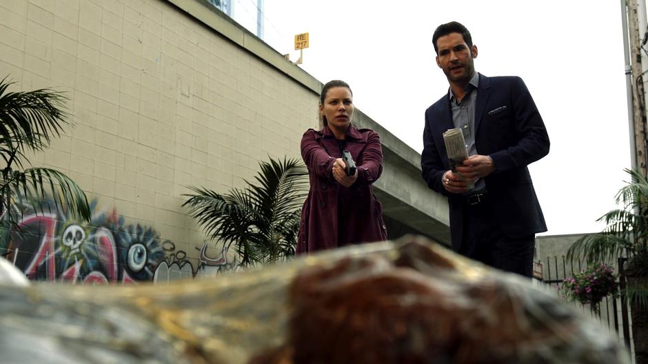 Chloe and Lucifer look down at the decomposing body wrapped in plastic.